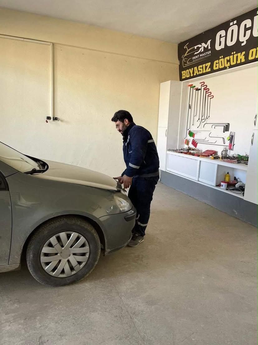 Sayed Sadat inspecting a dent on the hood of a gray hatchback, with PDR tools on the wall behind him