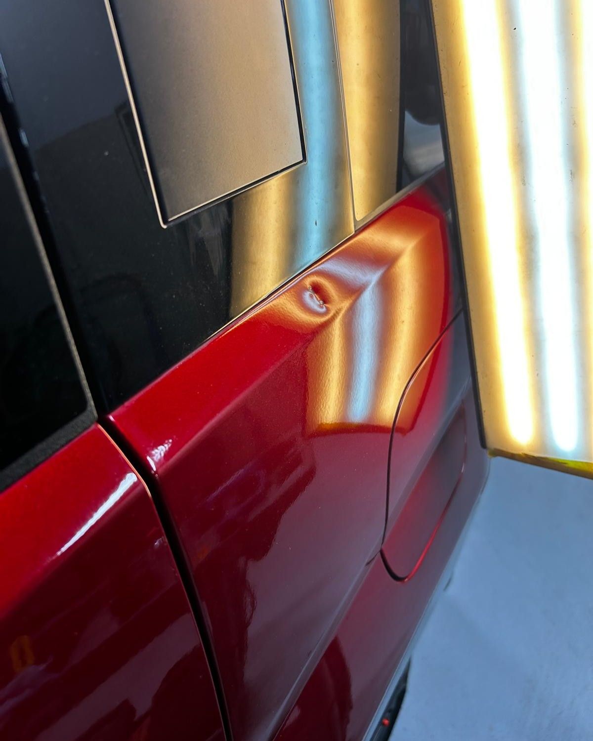 Before: small dent below the rear window on a red quarter panel, highlighted by a PDR light board